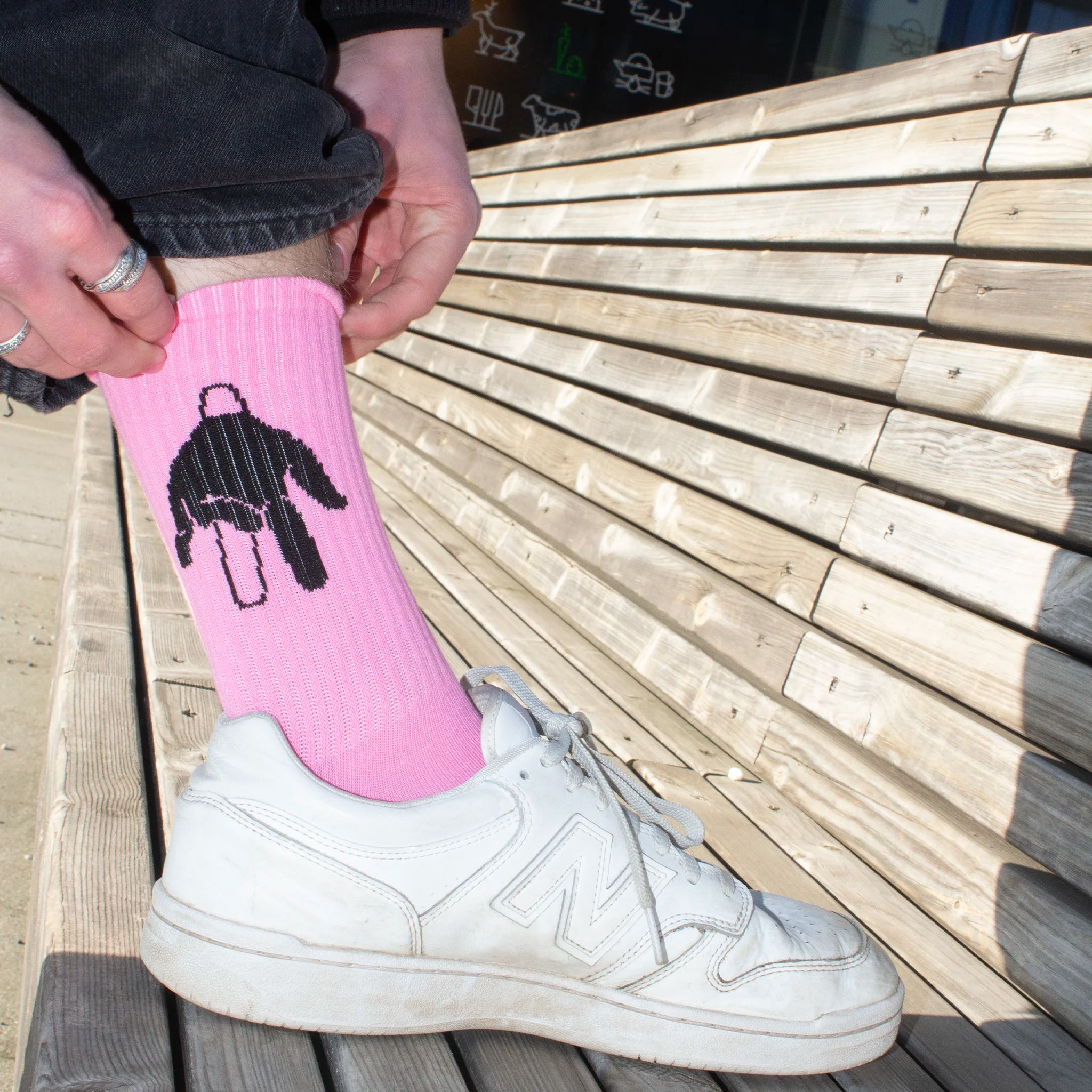 Person wearing a pink sock with a black design on a wooden bench